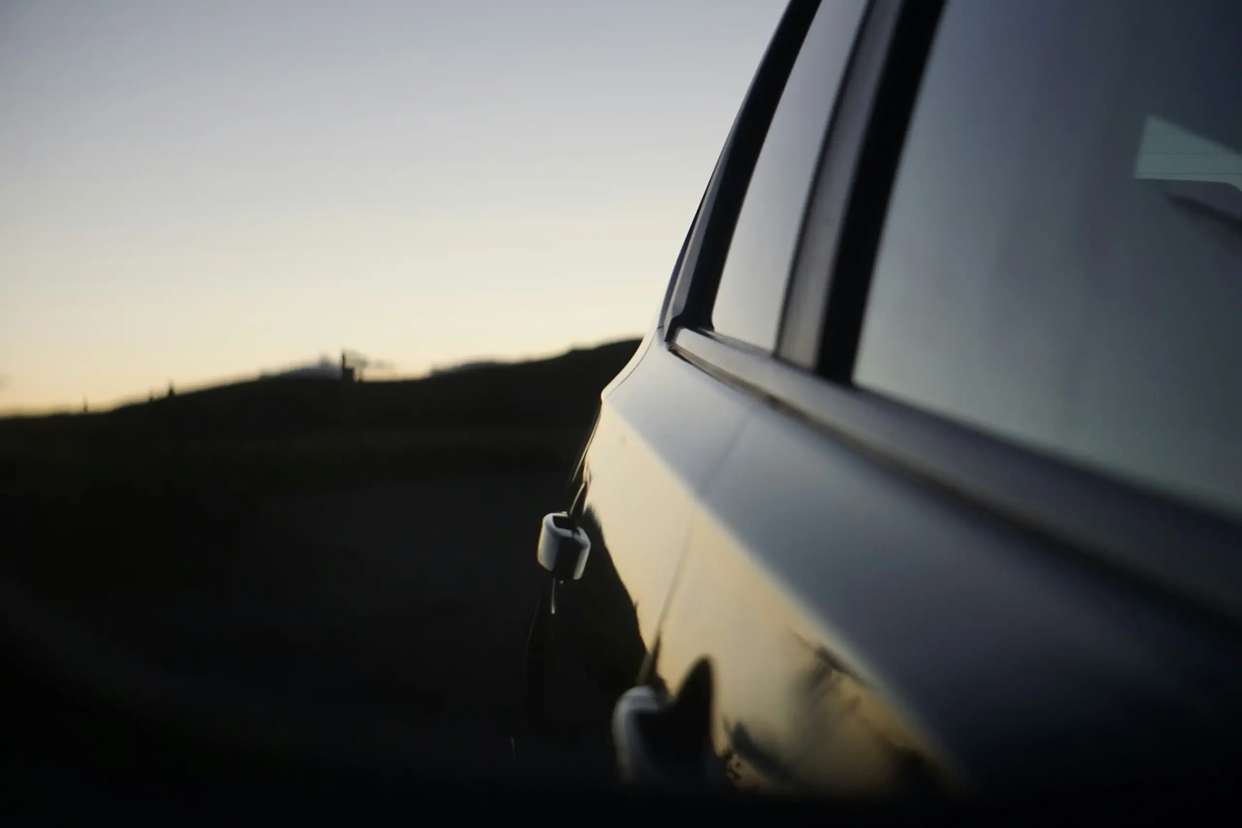 black luxury sedan parked curbside outside Boeing Field at sunrise, professional chauffeur in dark suit holding open rear door, private jet terminal in the background, crisp Pac...