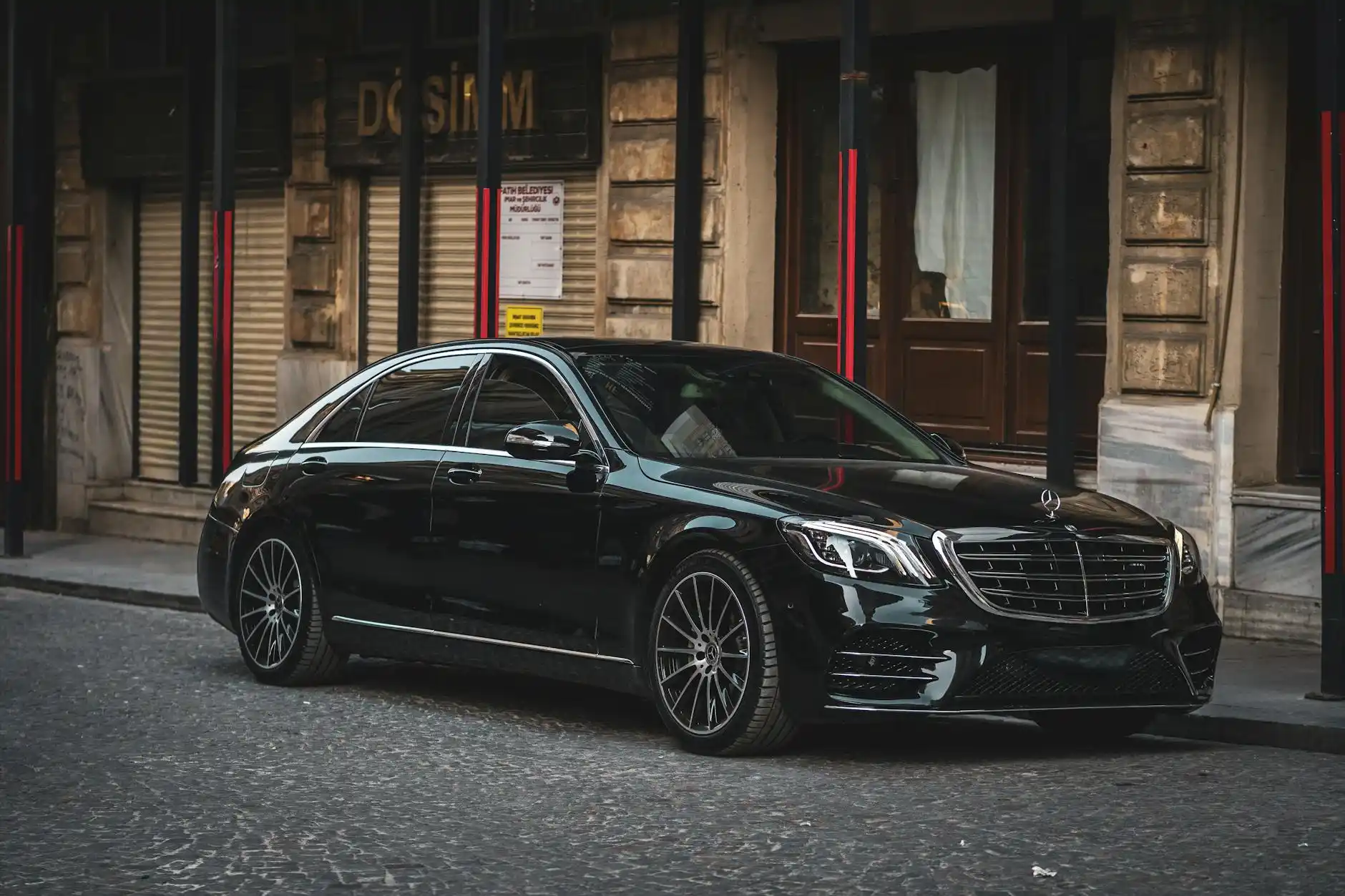black luxury sedan parked at Seattle-Tacoma International Airport curbside at sunrise, chauffeur opening the rear door, travelers with carry-on luggage, terminal glass reflectin...
