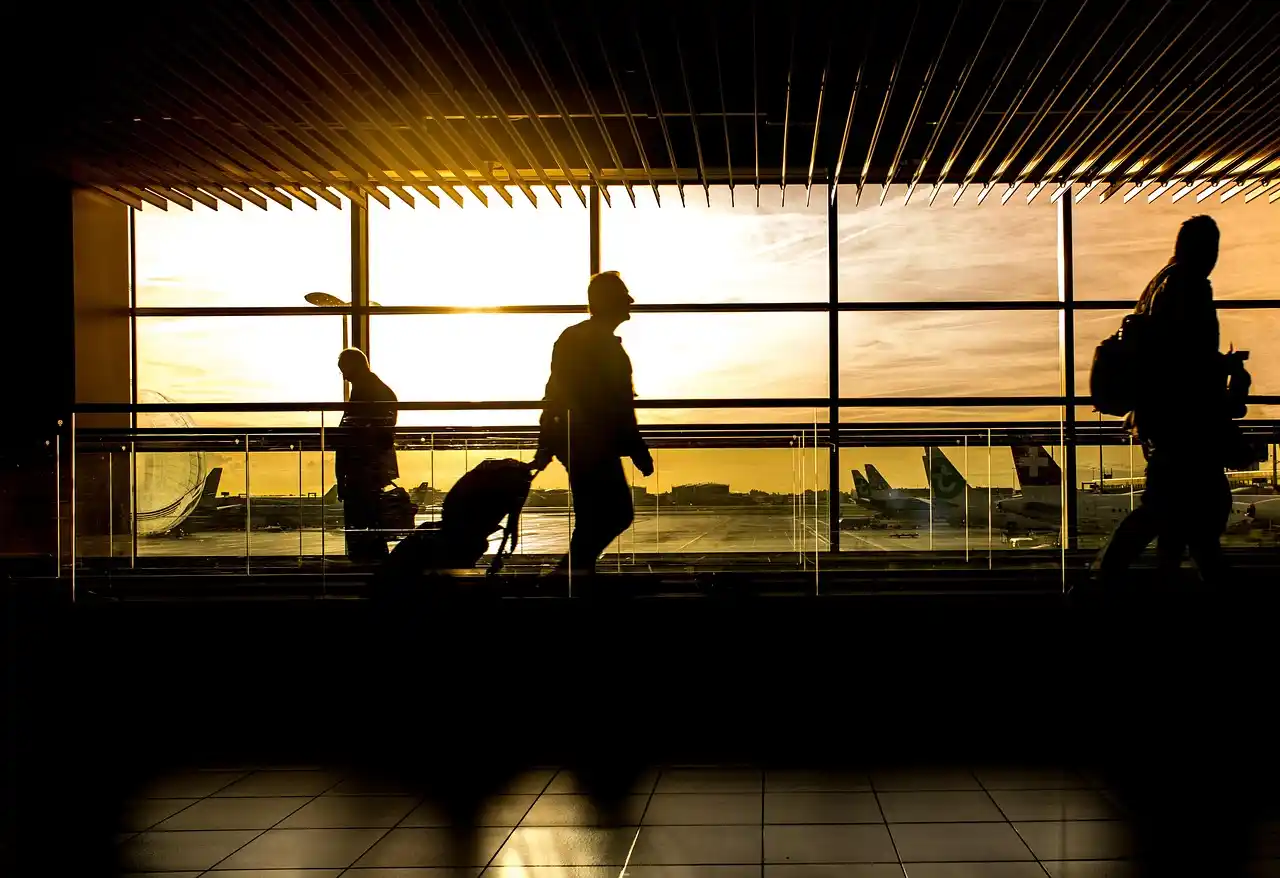 professional chauffeur in dark suit holding digital name sign inside SEA arrivals hall, polished floors, travelers walking by, warm overhead lighting and luggage carts nearby