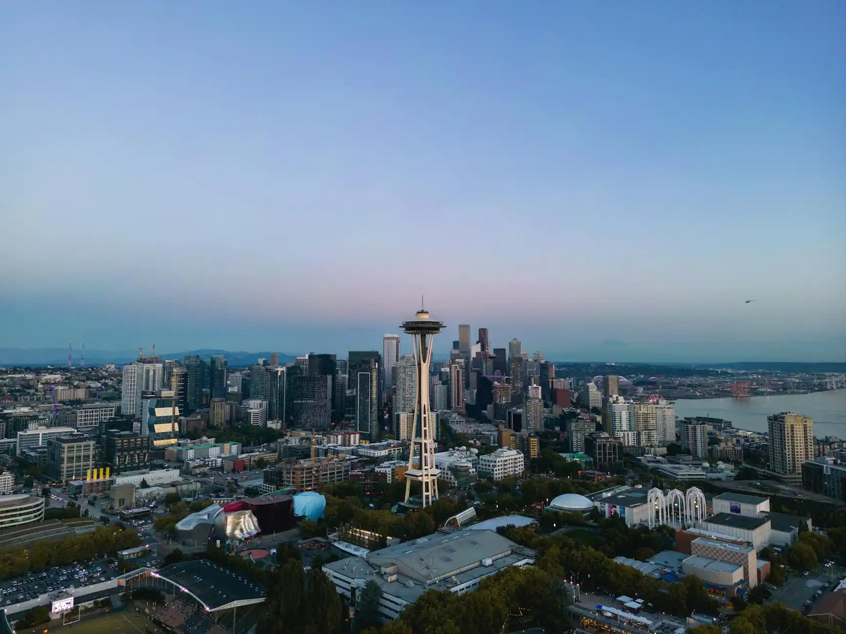 aerial view of Seattle freeway traffic near the airport at dusk, black executive car moving smoothly in a clear lane, SEA terminal and aircraft visible in the background
