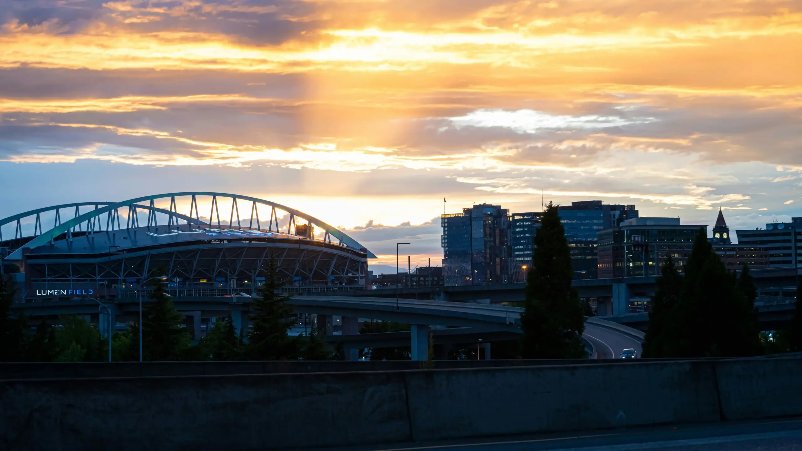 aerial view of Boeing Field and downtown Seattle traffic at sunset, private jet terminal visible, black town car traveling on a highway with city skyline and stadiums in the dis...