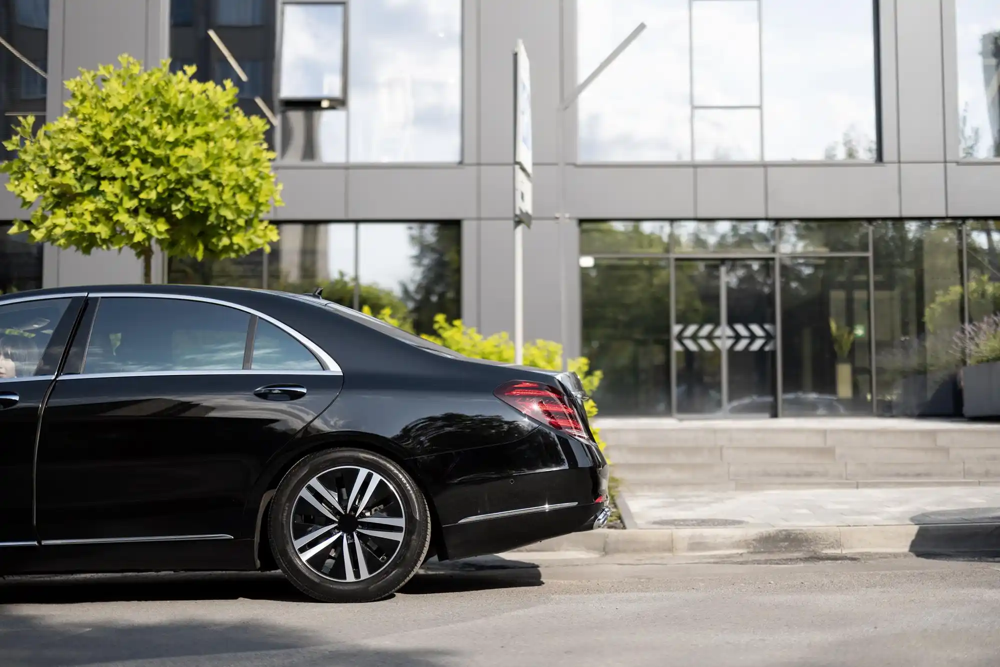 line of polished black executive sedans parked outside a Bellevue corporate campus, uniformed chauffeurs standing beside vehicles, overcast Pacific Northwest morning with modern...
