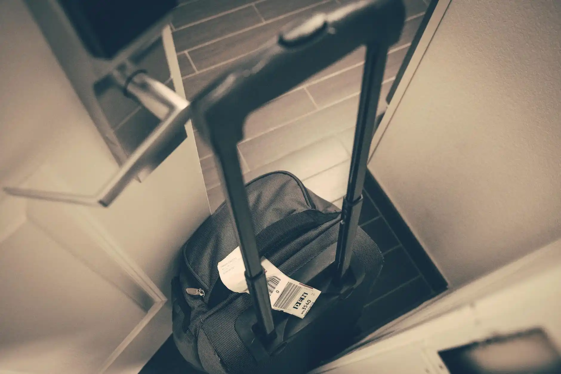traveler checking phone for airport ride confirmation in a quiet upscale home hallway at 4 a.m., packed suitcase by the door, warm interior lighting, realistic lifestyle photogr...