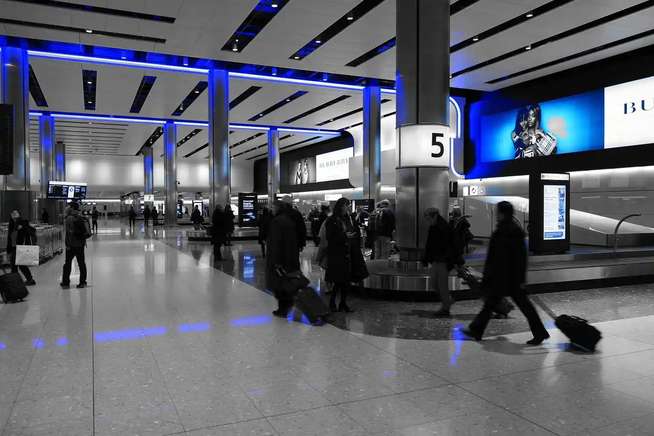nighttime arrivals scene at SeaTac airport baggage claim, well-dressed chauffeur holding digital name sign near escalators, traveler with rolling luggage approaching, polished m...