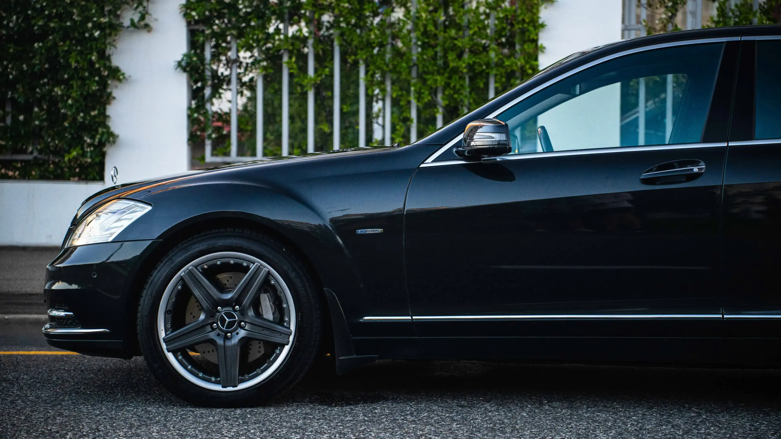 professionally dressed chauffeur in a black luxury sedan parked near Seattle waterfront at sunrise, Space Needle faintly visible in background, polished vehicle exterior, refine...