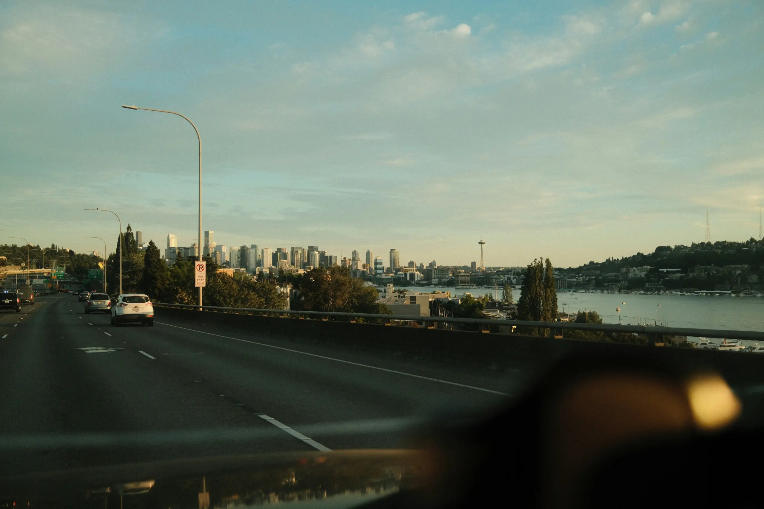 smartphone navigation on luxury car dashboard showing Seattle routes, chauffeur in suit driving carefully through downtown with soft rain outside and modern city skyline