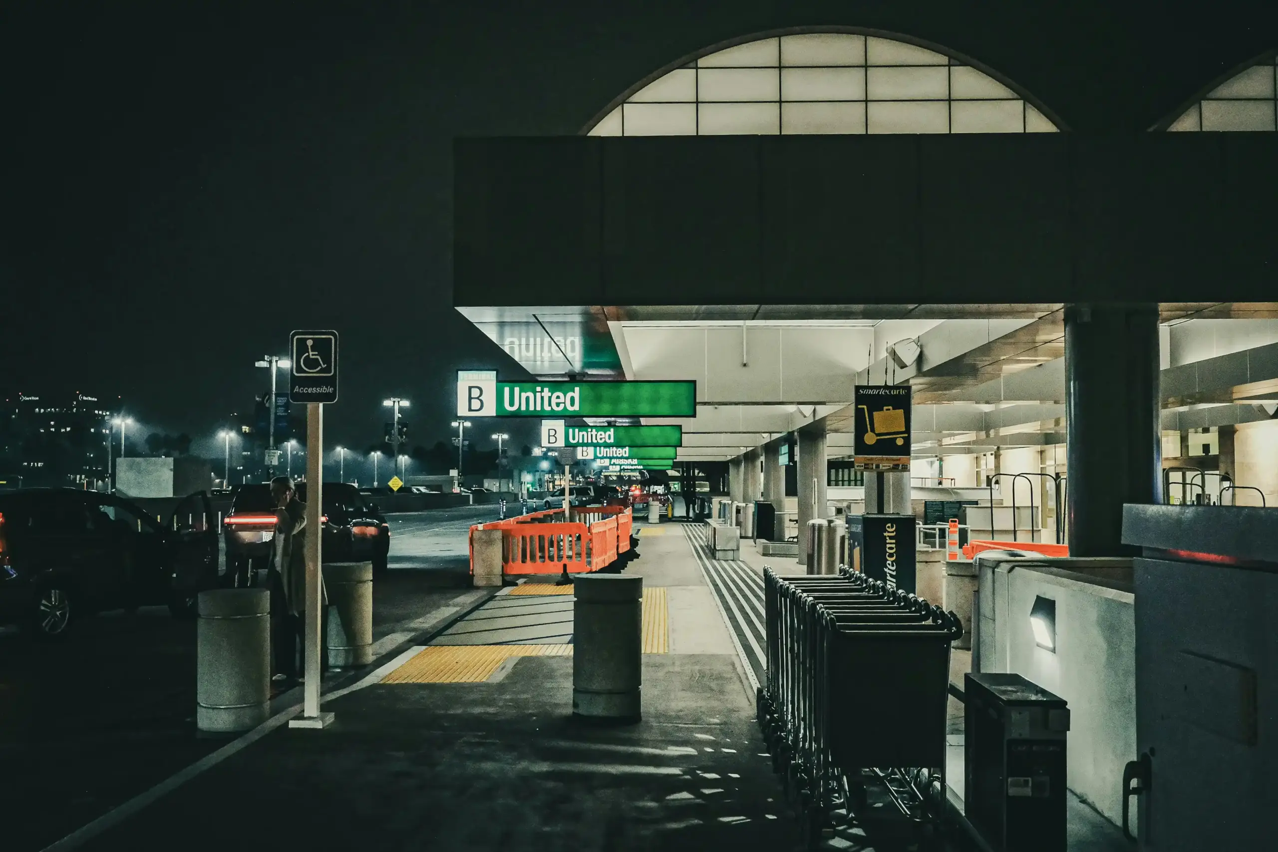 luxury chauffeur vehicle arriving at Seattle-Tacoma airport curbside at dusk, chauffeur assisting traveler with luggage, glowing terminal lights, wet pavement reflections