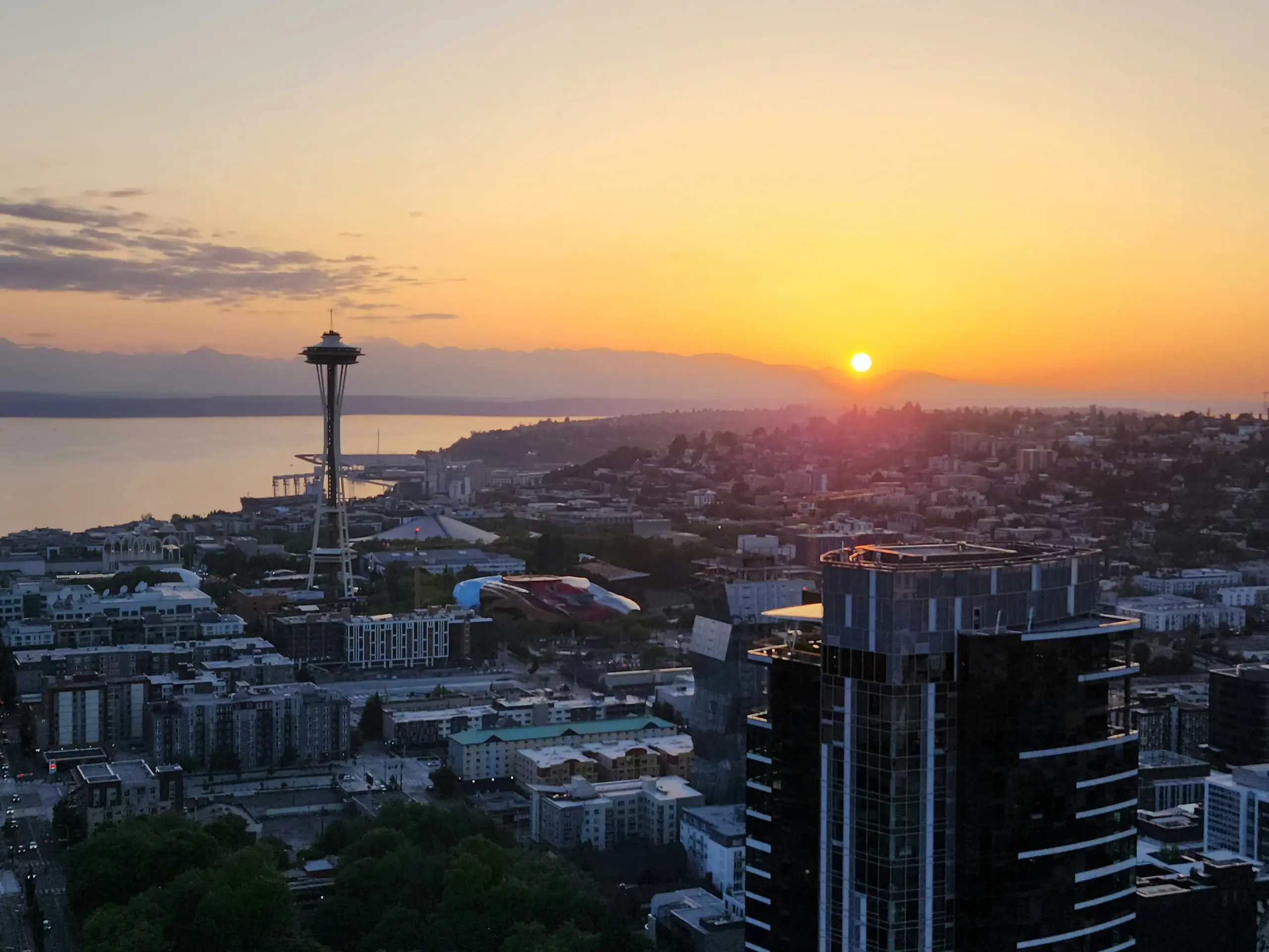 professional airport shuttle van picking up travelers outside a modern downtown Seattle hotel at sunrise, Space Needle faintly visible in the background, travelers with rolling ...