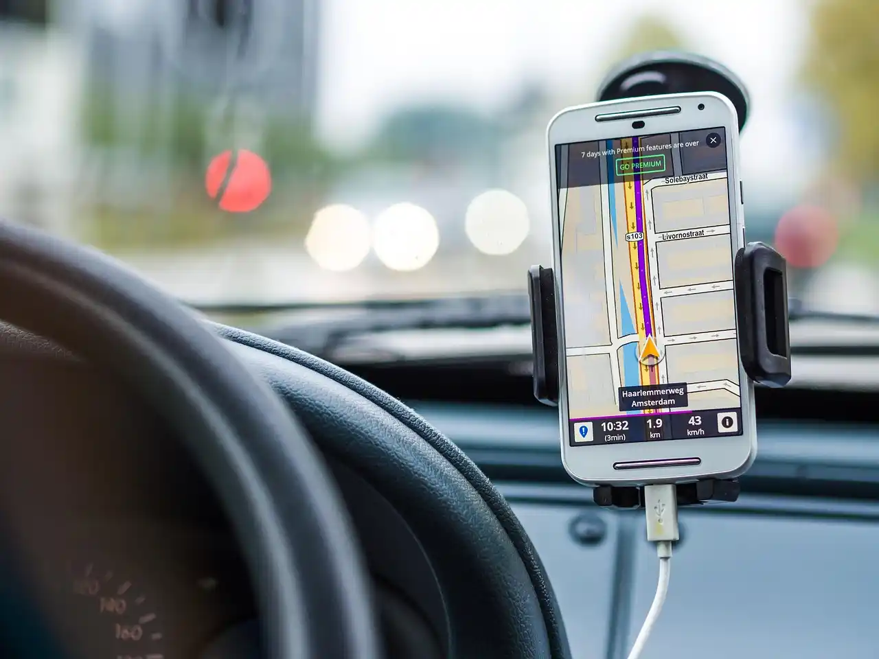 smartphone showing flight arrival updates next to a leather travel bag, chauffeur checking route on navigation screen inside a clean executive vehicle, rainy Seattle streets out...