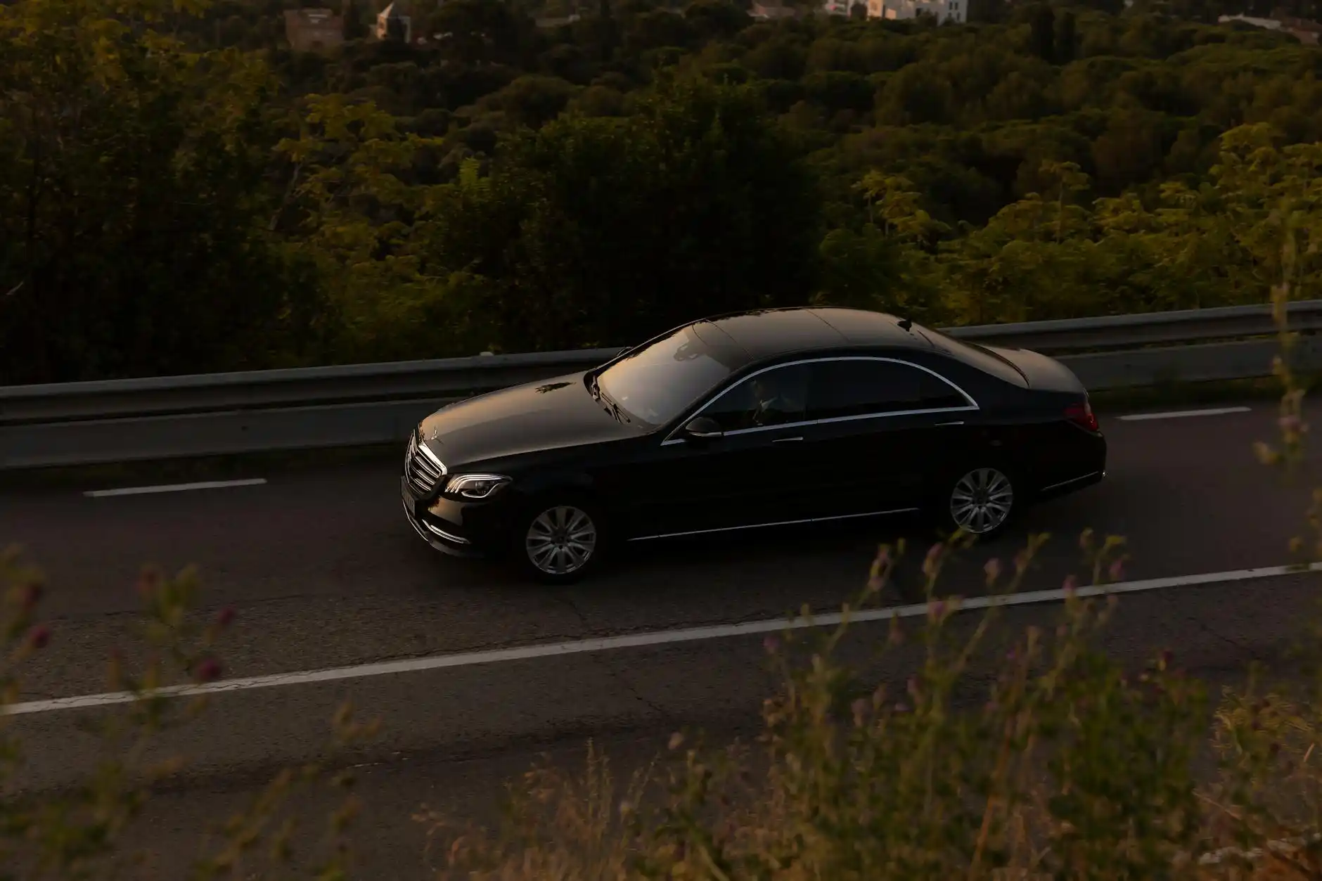 black luxury sedan traveling along a tree-lined Bellevue boulevard with tinted windows, soft overcast light, upscale residential surroundings, sense of privacy and quiet motion