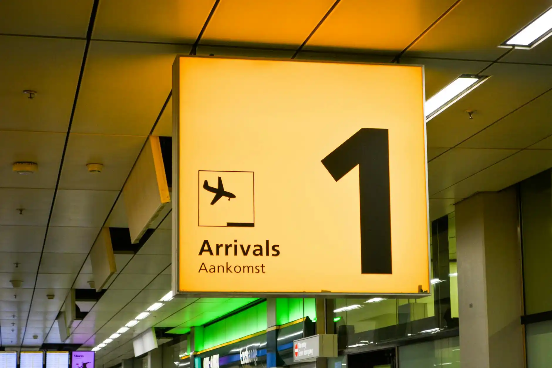 professional airport pickup scene at SeaTac arrivals, chauffeur holding digital name sign beside luxury black sedan, evening terminal lights reflecting on wet pavement, traveler...