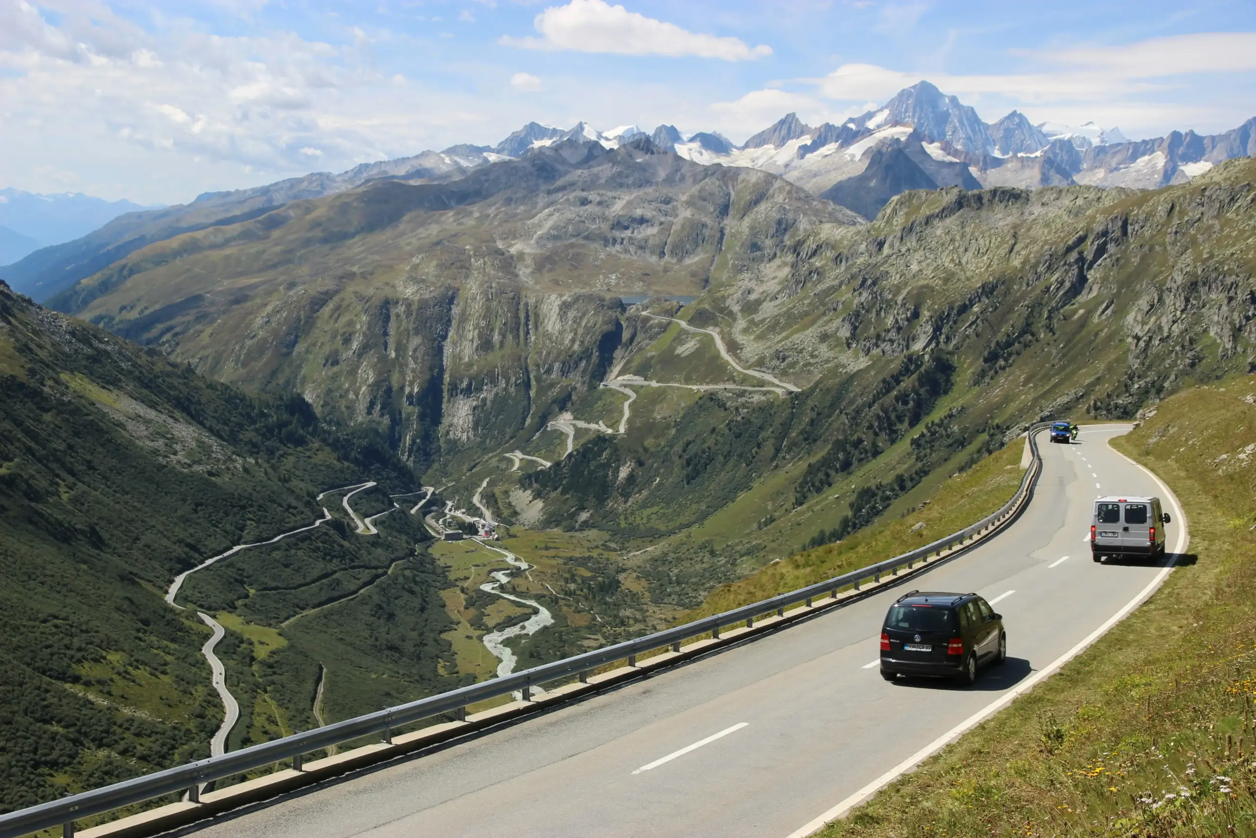 executive passengers seated in a black luxury SUV crossing a border checkpoint, passports ready, with mountain views and organized travel bags inside