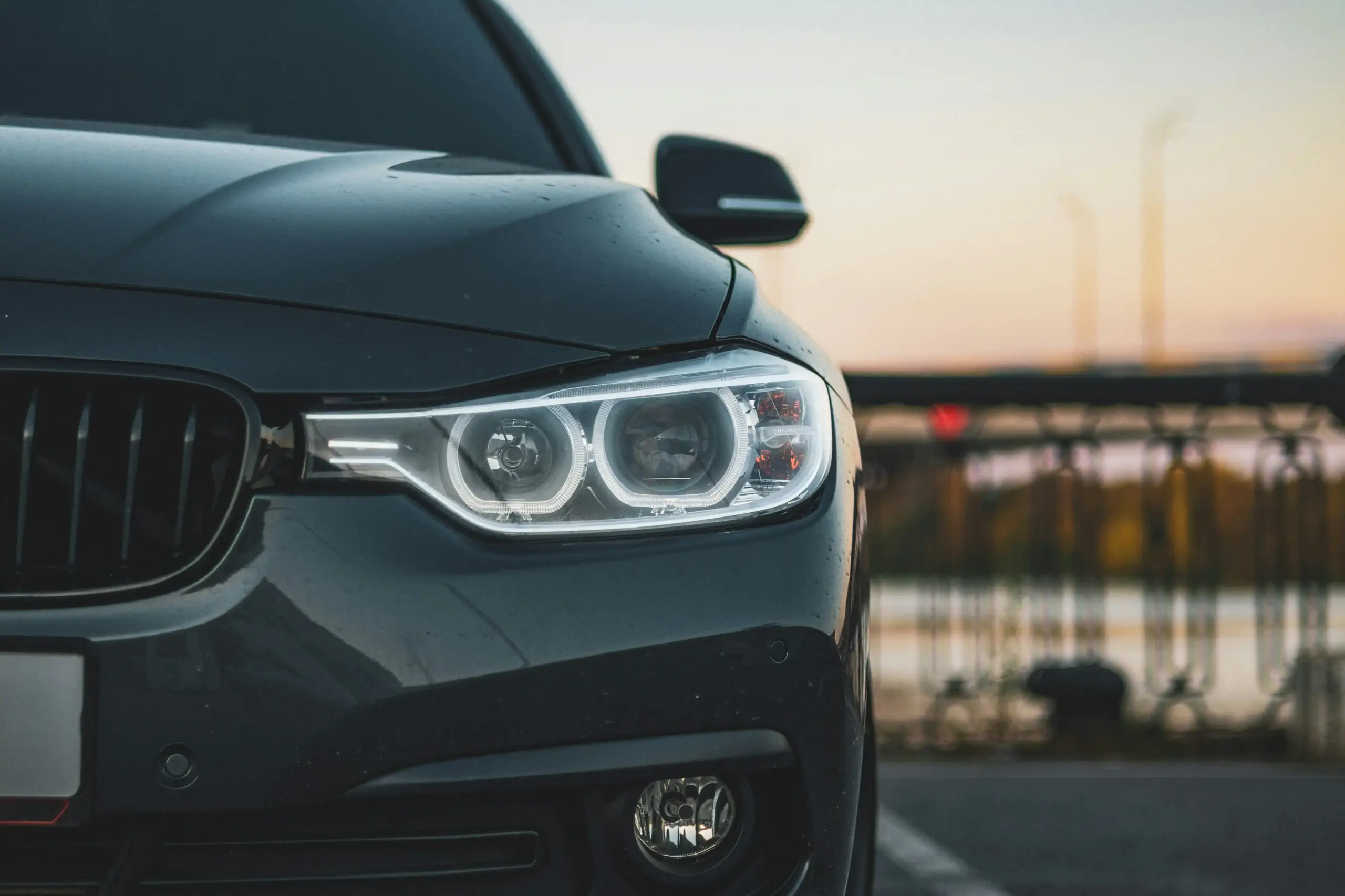 black executive sedan driving along the coastal highway toward Vancouver at golden hour, evergreen trees, distant mountains, and clean city skyline ahead