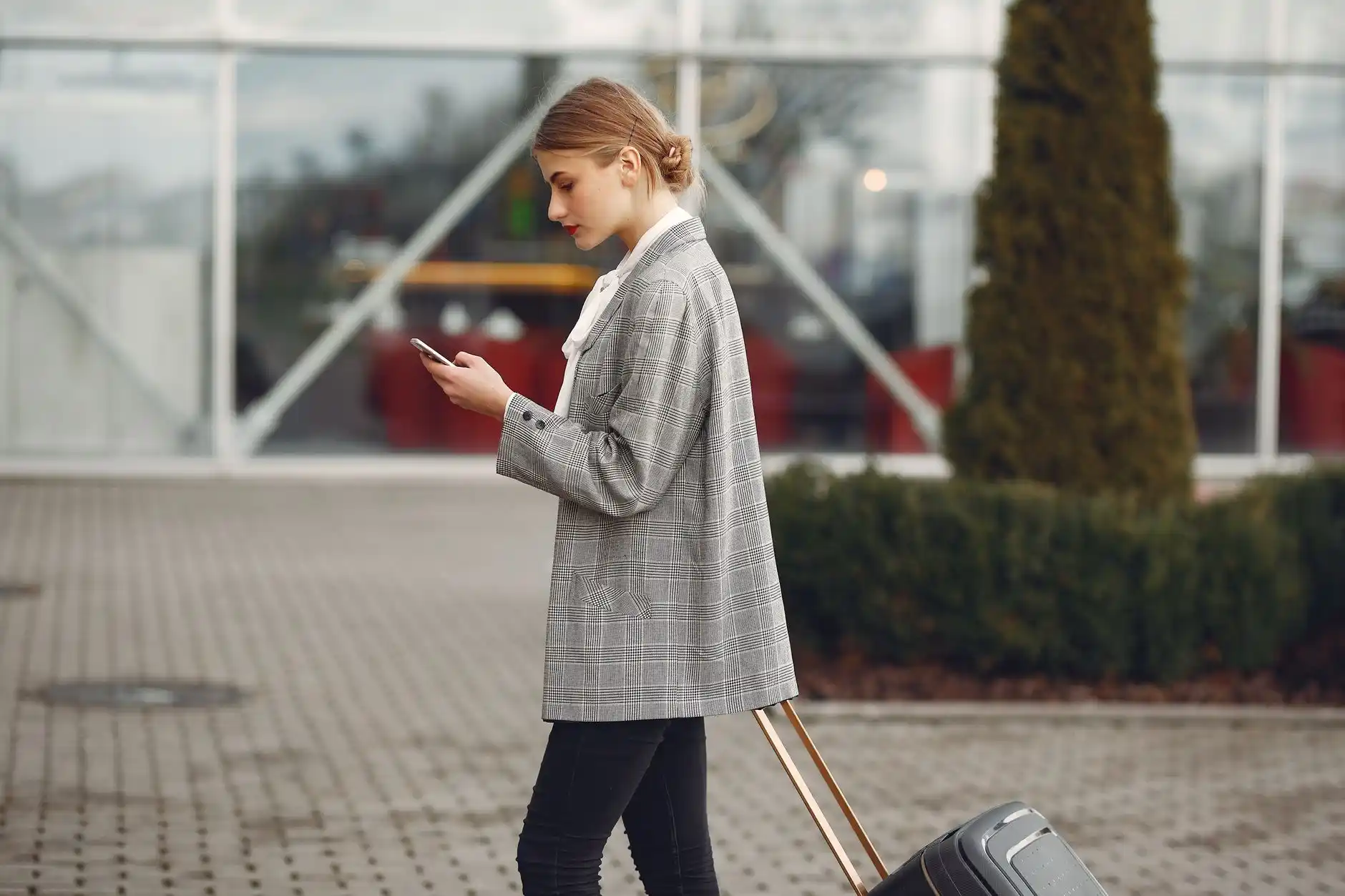 traveler at home entryway in Bellevue checking flight details on smartphone while chauffeur loads suitcases into a black SUV parked in driveway, soft morning light and evergreen...