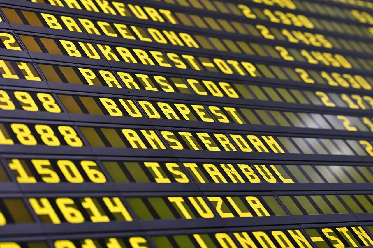 airport arrivals scene at Seattle-Tacoma International Airport, chauffeur holding a name sign near baggage claim, flight information board showing delayed arrival