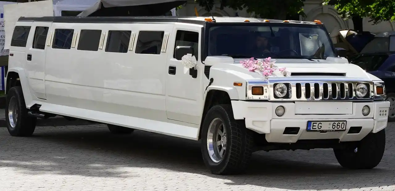 elegant Seattle wedding couple entering a white luxury limousine outside a waterfront venue at sunset, floral arrangements and city skyline in background