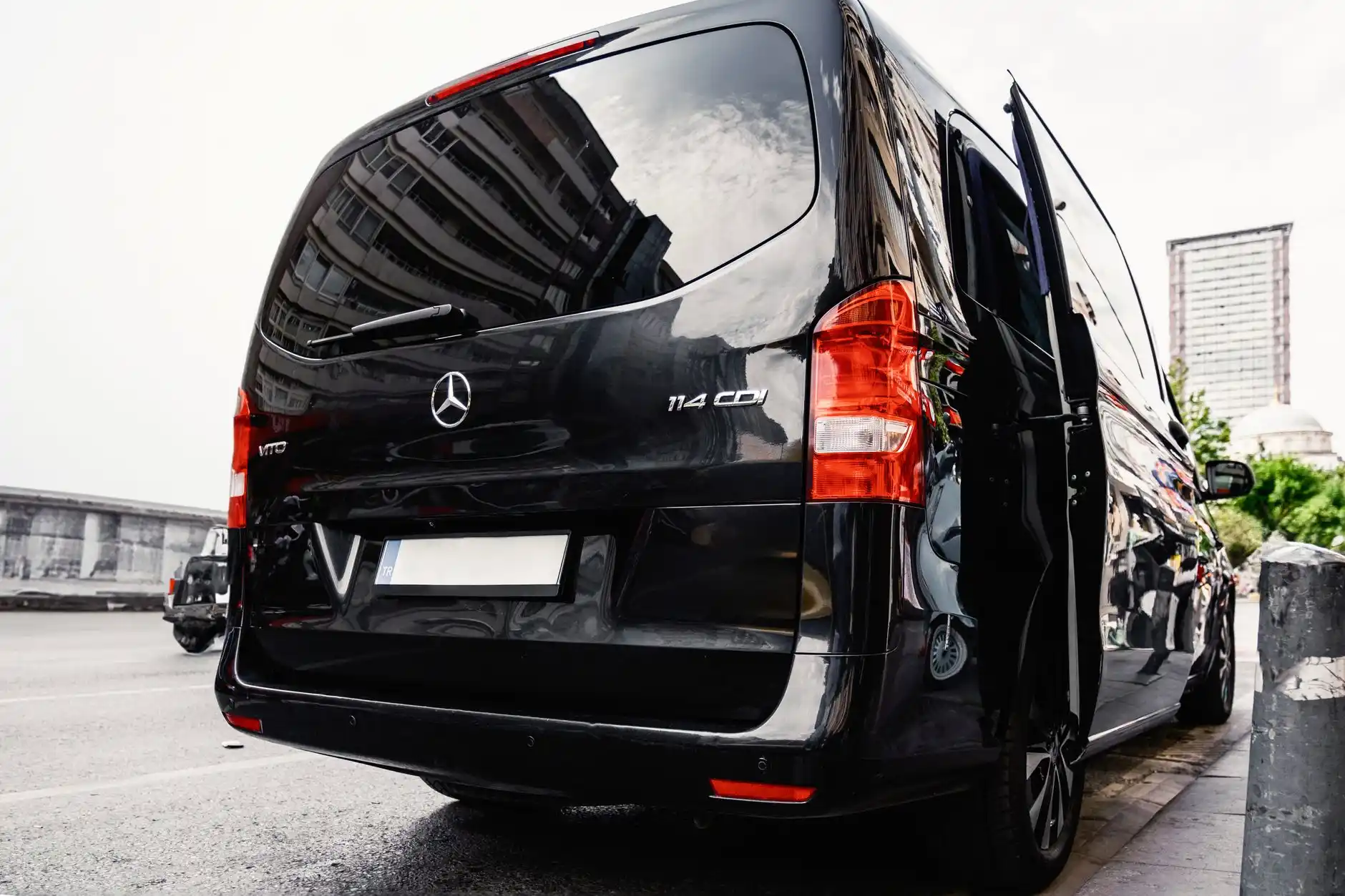 black luxury sprinter van parked curbside at an upscale hotel entrance, side door open to show spacious leather seating for 14 passengers, soft interior lighting, luggage visibl...